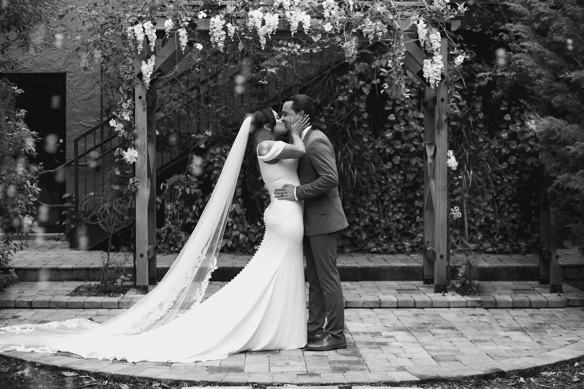 Bride and groom kissing under a wisteria arbor